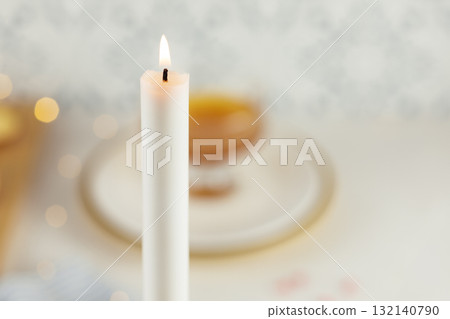 A burning white candle on a blurry kitchen background with table setting, honey and lights. Rosh hashanah, Jewish New Year holiday. Selective focus. Jewish holiday background A burning white candle on a blurry kitchen background with table setting, honey and lights. Rosh hashanah, Jewish New Year holiday. Selective focus. Jewish holiday background 132140790