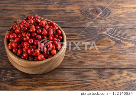 red dog-rose rosehip fruits in a wooden bowl on wooden table 132140824
