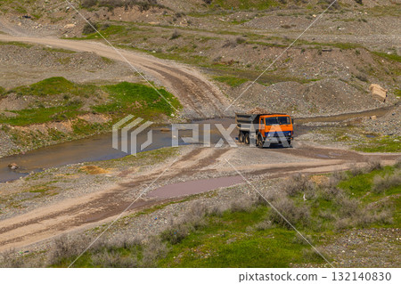 Truck loaded with rocks driving through stream in rural mountainous area Truck loaded with rocks driving through stream in rural mountainous area 132140830