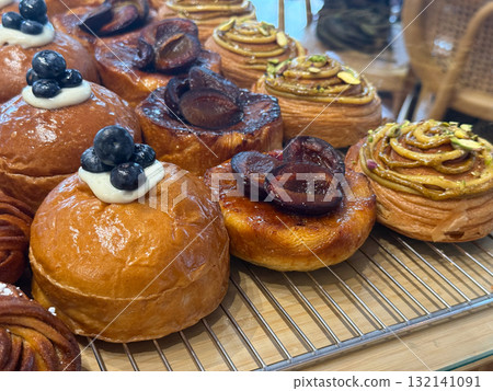 Round buns with cream and blueberries placed between almond croissants and pistachio rolls. Bakery assortment symbolizing flavor, color, and craftsmanship. 132141091