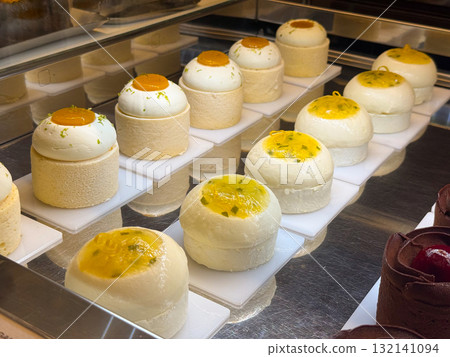 Round mousse cakes topped with mango glaze placed in a pastry display. Dessert presentation symbolizing freshness, softness, and bakery refinement. 132141094