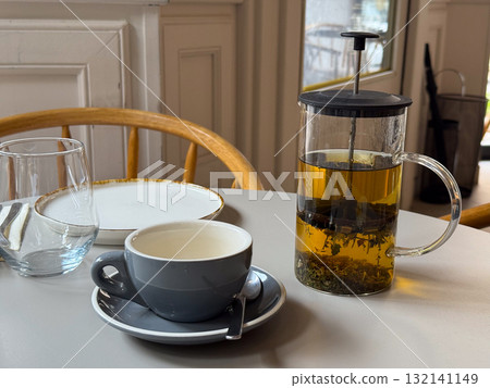 Teapot with herbal tea and cup on a cafe table. Warm beverage, relaxation and cozy urban lifestyle. Teapot with herbal tea and cup on a cafe table. Warm beverage, relaxation and cozy urban lifestyle. 132141149