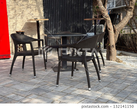 Rattan chairs and small tables arranged on tiled pavement in sunny courtyard. Peaceful scene reflecting urban relaxation and slow rhythm of life. Rattan chairs and small tables arranged on tiled pavement in sunny courtyard. Peaceful scene reflecting urban relaxation and slow rhythm of life. 132141150