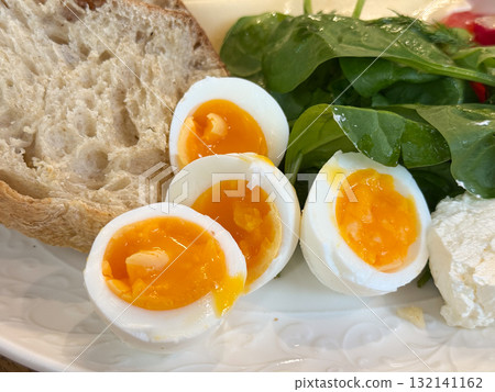 Slices of bread and halved eggs arranged on white plate with fresh greens. Simple breakfast scene showing warmth and nourishment. Slices of bread and halved eggs arranged on white plate with fresh greens. Simple breakfast scene showing warmth and nourishment. 132141162