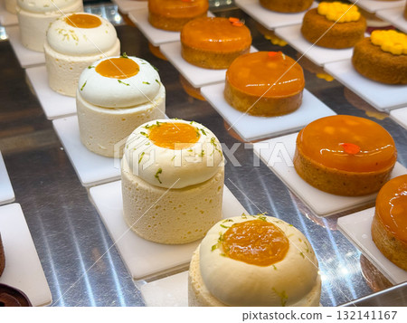 Small mousse cakes with citrus topping placed on white plates. Bakery presentation highlighting detail, structure, and refined pastry craft. Small mousse cakes with citrus topping placed on white plates. Bakery presentation highlighting detail, structure, and refined pastry craft. 132141167