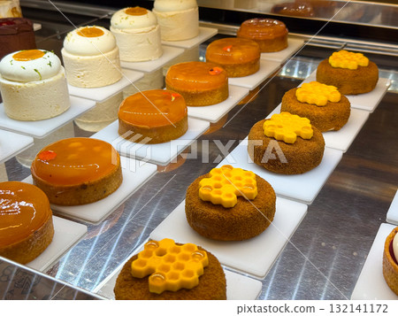Variety of round pastries with honey decoration and citrus glaze on display counter. Artistic presentation showing detail, structure, and precision in modern confectionery design. Variety of round pastries with honey decoration and citrus glaze on display counter. Artistic presentation showing detail, structure, and precision in modern confectionery design. 132141172