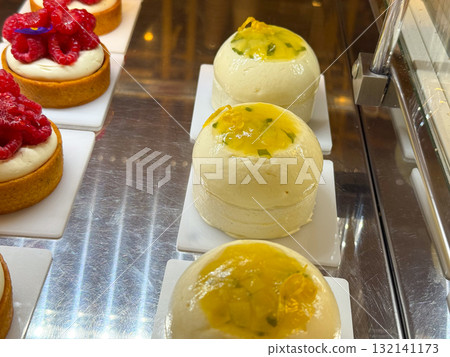 Round mousse cakes topped with mango glaze placed in a pastry display. Dessert presentation symbolizing freshness, softness, and bakery refinement. Round mousse cakes topped with mango glaze placed in a pastry display. Dessert presentation symbolizing freshness, softness, and bakery refinement. 132141173