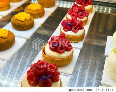 Small tartlets filled with cream and fresh raspberries arranged on white plates. Bakery display reflecting precision, sweetness, and vibrant dessert presentation. Small tartlets filled with cream and fresh raspberries arranged on white plates. Bakery display reflecting precision, sweetness, and vibrant dessert presentation. 132141174
