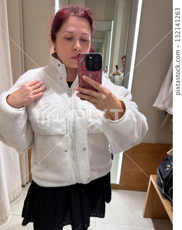 Trying on a white jacket in a fitting room. Exploration of personal style, body confidence, and fashion self-expression through casual minimalism and neutral tones. Trying on a white jacket in a fitting room. Exploration of personal style, body confidence, and fashion self-expression through casual minimalism and neutral tones. 132141263
