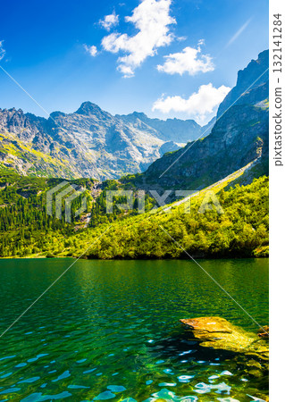 travel mountain landscape with lake in summer. green water of morskie oko in high tatra. beauty in nature park of poland. forest on the rocky slope. beautiful view of alpine pond on a sunny day travel mountain landscape with lake in summer. green water of morskie oko in high tatra. beauty in nature park of poland. forest on the rocky slope. beautiful view of alpine pond on a sunny day 132141284