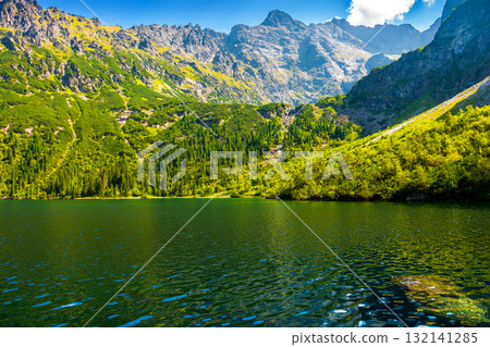 travel mountain landscape with lake in summer. green water of morskie oko in high tatra. beauty in nature park of poland. forest on the rocky slope. beautiful view of alpine pond on a sunny day 132141285