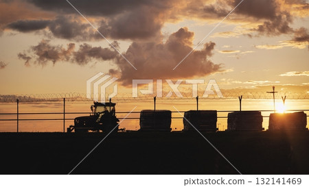 Airport tractor silhouette at sunset with razor wire fence and dramatic clouds 132141469