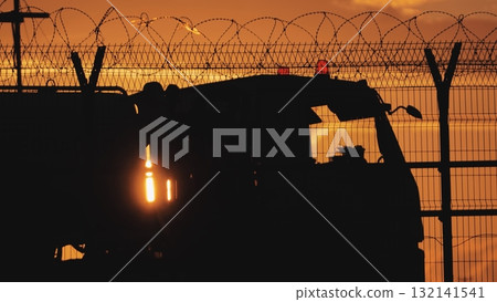 Airport service truck passing behind barbed wire fence at sunset Airport service truck passing behind barbed wire fence at sunset 132141541