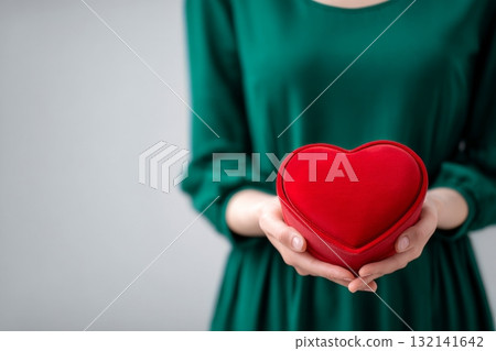 Woman in Green Dress Holds Red Heart-Shaped Box Against Gray Background During a Romantic Moment 132141642