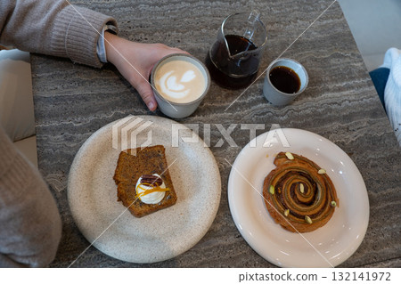 Top view of a cozy coffee break with latte art, black coffee, carrot cake slice, and pistachio pastry on a stone table 132141972
