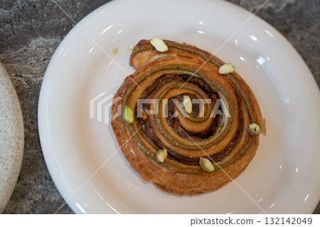 Fresh pistachio pastry served on a white plate with a cup of black coffee in a modern cafe Fresh pistachio pastry served on a white plate with a cup of black coffee in a modern cafe 132142049