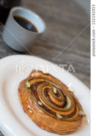 Fresh pistachio pastry served on a white plate with a cup of black coffee in a modern cafe 132142053
