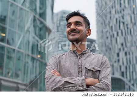 Man Smiling Confidently in Modern Cityscape Against Glass Building Backdrop in Overcast Weather 132142116