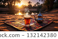 Steaming glass of mint tea and a teapot on a mat in the desert during a beautiful sunset 132142380