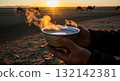 Hands holding a traditional mongolian suutei tsai milk tea with camels in the desert at sunset 132142381