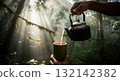 Pouring hot toasted rice tea into a bamboo cup in a misty jungle with morning sunbeams 132142382