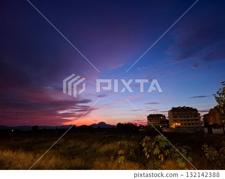 This stunning sunset in southern Spain features a blend of orange, pink, and purple hues filling the sky. Buildings softly outline the horizon, creating a serene scene. 132142388