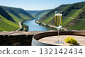 Glass of sparkling cremant wine and grapes on a barrel overlooking a river valley vineyard 132142434