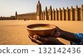 Person holding a bowl of ginger juice in front of a great mud-brick mosque in Africa 132142436
