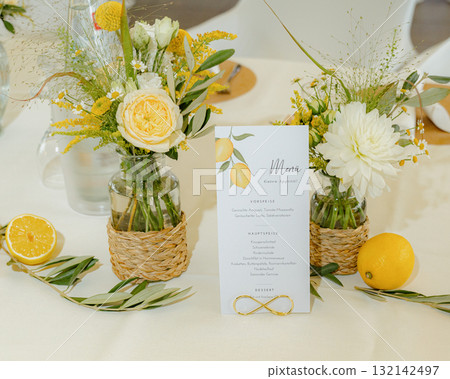 Beautiful table setting featuring vibrant floral arrangements in woven vases, complemented by a menu card adorned with lemon illustrations. Fresh lemons and greenery enhance the scene Beautiful table setting featuring vibrant floral arrangements in woven vases, complemented by a menu card adorned with lemon illustrations. Fresh lemons and greenery enhance the scene 132142497