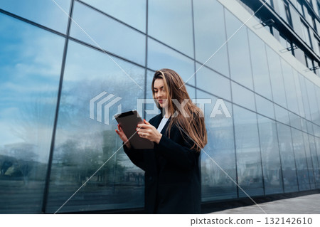 Young Woman Using Tablet Outside Modern Building With Reflective Glass During Daytime in an Urban Environment 132142610