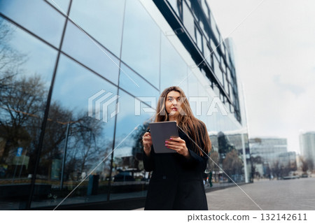 Young Woman Using Tablet While Standing on Urban Street With Modern Buildings and Reflection During a Clear Day Young Woman Using Tablet While Standing on Urban Street With Modern Buildings and Reflection During a Clear Day 132142611