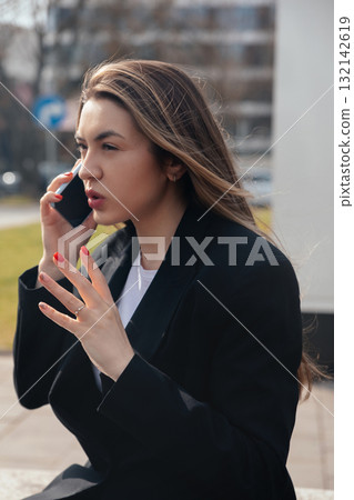Woman Engaged in a Phone Conversation Outdoors While Gesturing With Her Hands in a Busy Urban Setting During Daylight Woman Engaged in a Phone Conversation Outdoors While Gesturing With Her Hands in a Busy Urban Setting During Daylight 132142619