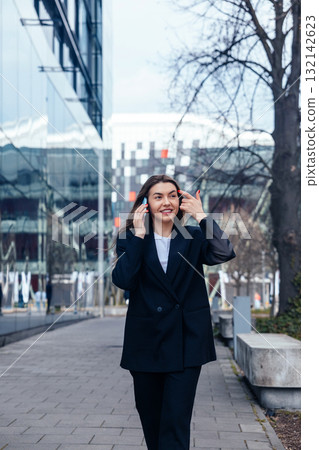 Businesswoman Walking Confidently on Urban Street While Talking on Her Phone During a Sunny Day in a Modern City Environment Businesswoman Walking Confidently on Urban Street While Talking on Her Phone During a Sunny Day in a Modern City Environment 132142623
