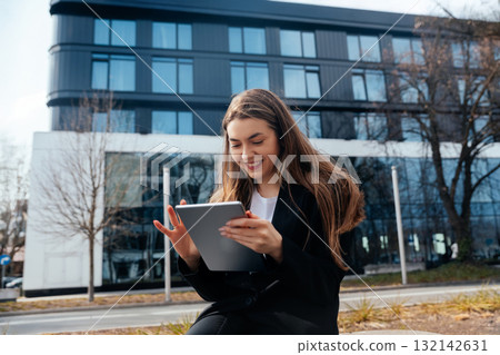 Young woman using tablet outdoors, enjoying technology in a modern urban environment, smiling and engaged with device, lifestyle concept 132142631