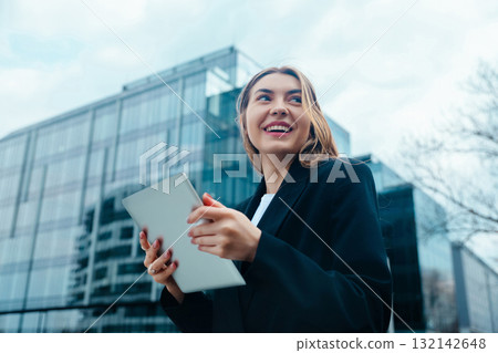 Professional woman smiling while holding tablet outdoors in urban setting with modern architecture showcasing technology and connectivity concept Professional woman smiling while holding tablet outdoors in urban setting with modern architecture showcasing technology and connectivity concept 132142648