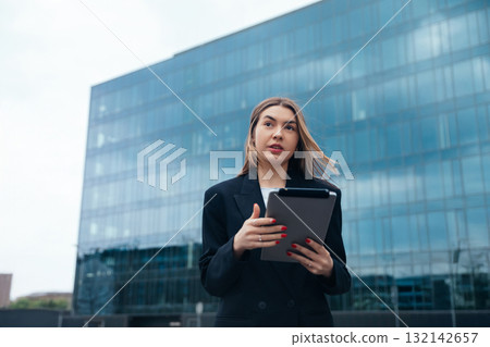 Businesswoman holding tablet outdoors in urban setting with modern architecture in background showcasing professional attire and confident expression technology concept Businesswoman holding tablet outdoors in urban setting with modern architecture in background showcasing professional attire and confident expression technology concept 132142657