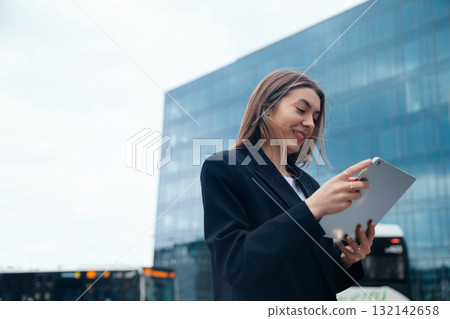 Professional woman using tablet outdoors in urban setting with modern architecture in background showcasing technology and connectivity concept 132142658