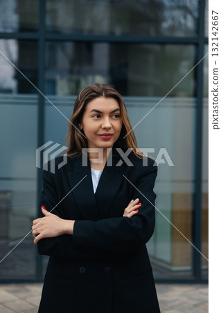 Confident young woman in stylish black blazer standing with arms crossed, showcasing modern urban background, professional demeanor, business fashion concept Confident young woman in stylish black blazer standing with arms crossed, showcasing modern urban background, professional demeanor, business fashion concept 132142667