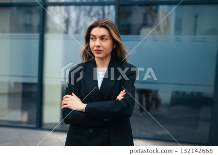 Confident young woman in a stylish black blazer standing with arms crossed, showcasing a modern urban background, professional attitude, empowerment concept Confident young woman in a stylish black blazer standing with arms crossed, showcasing a modern urban background, professional attitude, empowerment concept 132142668