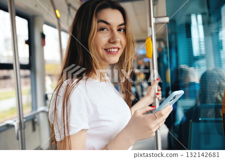 Young woman smiling while holding smartphone in public transport, enjoying her journey, modern lifestyle concept Young woman smiling while holding smartphone in public transport, enjoying her journey, modern lifestyle concept 132142681