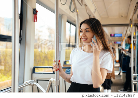 Young woman smiling while talking on smartphone inside public transport, enjoying her commute, urban lifestyle concept 132142687