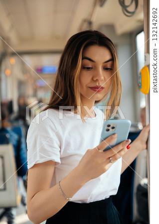 Young woman using smartphone while commuting on public transport, engaged in social media interaction, urban lifestyle concept Young woman using smartphone while commuting on public transport, engaged in social media interaction, urban lifestyle concept 132142692