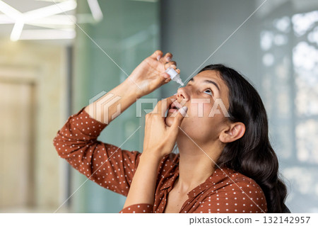 Young woman applying eye drops, providing ocular relief and maintaining vision health, addressing eye irritation, allergy symptoms, or dry eye syndrome with a therapeutic solution 132142957