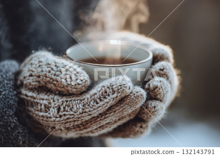 Hands in knitted mittens holding cup outdoors on cold winter day 132143791
