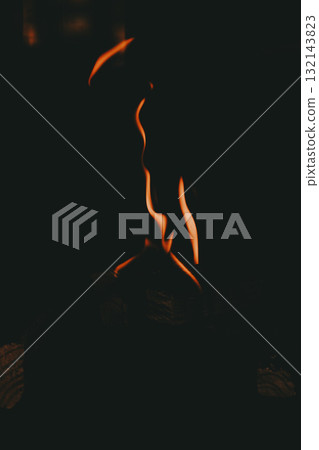 Dark minimalistic shot of orange flames rising in the darkness, abstract fire shapes dancing above burning wood Dark minimalistic shot of orange flames rising in the darkness, abstract fire shapes dancing above burning wood 132143823