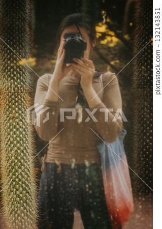 Photographer Capturing the Moment in a Botanical Garden. A woman is taking a photo with a camera, framed by a cactus. 132143851