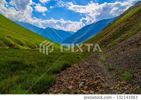 Majestic mountain landscape with grassy fields and rocky path in Kyrgyzstan 132143863