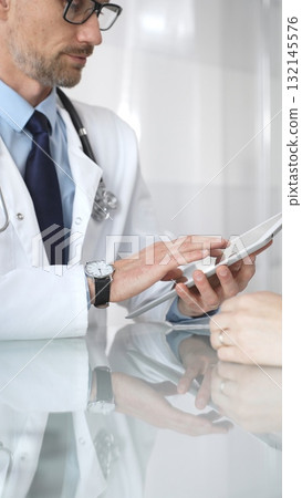 Male doctor consulting female patient, discussing diagnosis and medical history with digital tablet in clinic. Medicine and health care 132145576