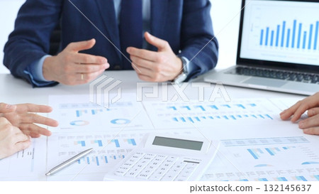 Business professionals collaborating at a conference table, reviewing financial charts and reports, using a laptop and calculator while engaging in discussions about strategy and performance 132145637