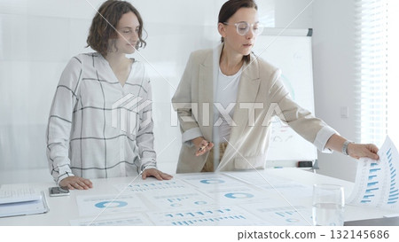 Two businesswomen are examining financial charts and statistics during a productive meeting in a modern office, demonstrating teamwork and strategic planning. Business people concept Two businesswomen are examining financial charts and statistics during a productive meeting in a modern office, demonstrating teamwork and strategic planning. Business people concept 132145686